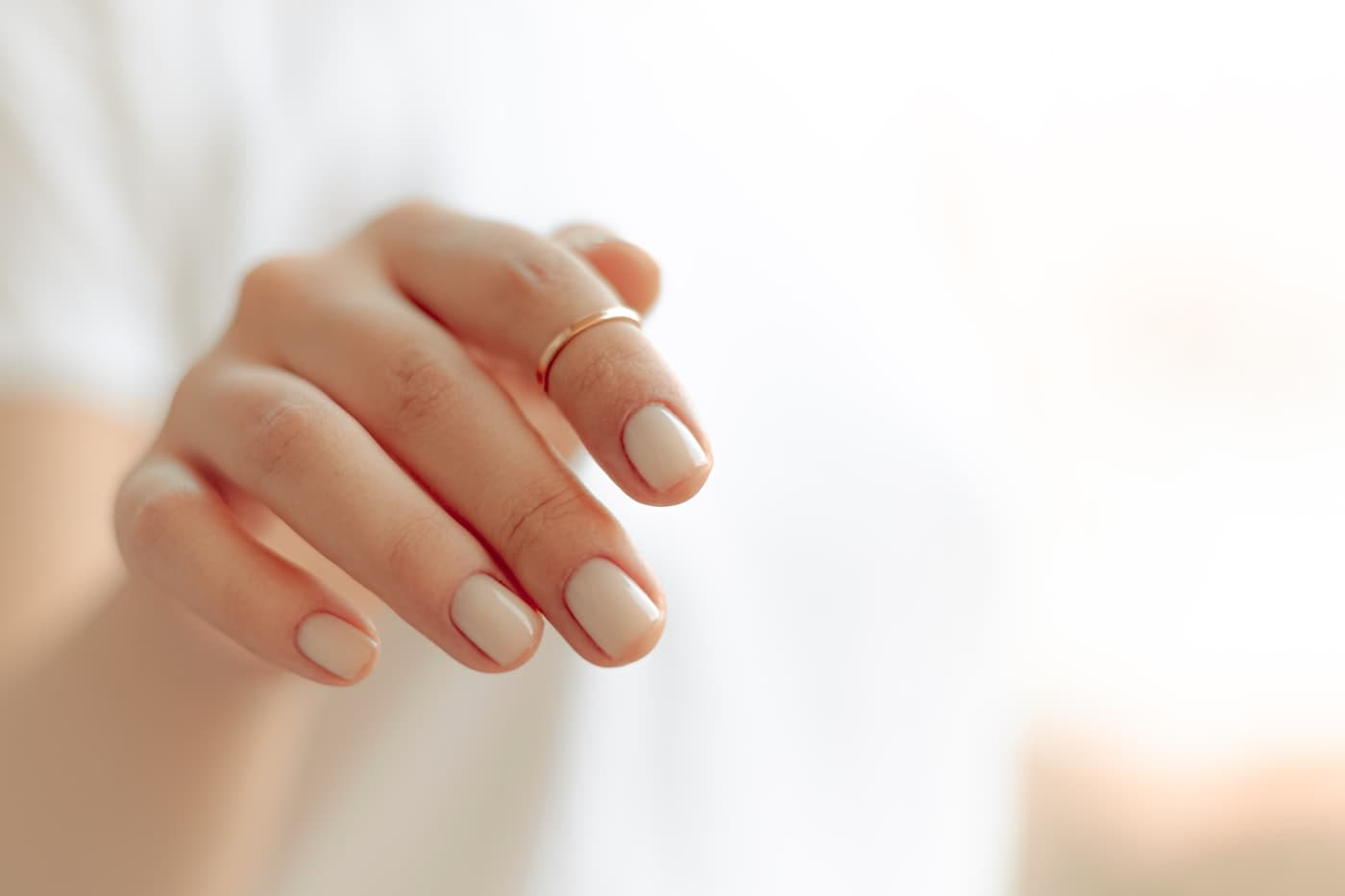 A hand with a soft nude manicure in bright daylight