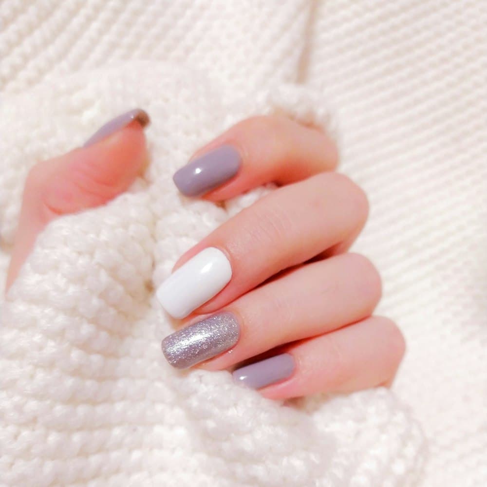 A hand with grey, white and silver shimmer nails on a knit sweater